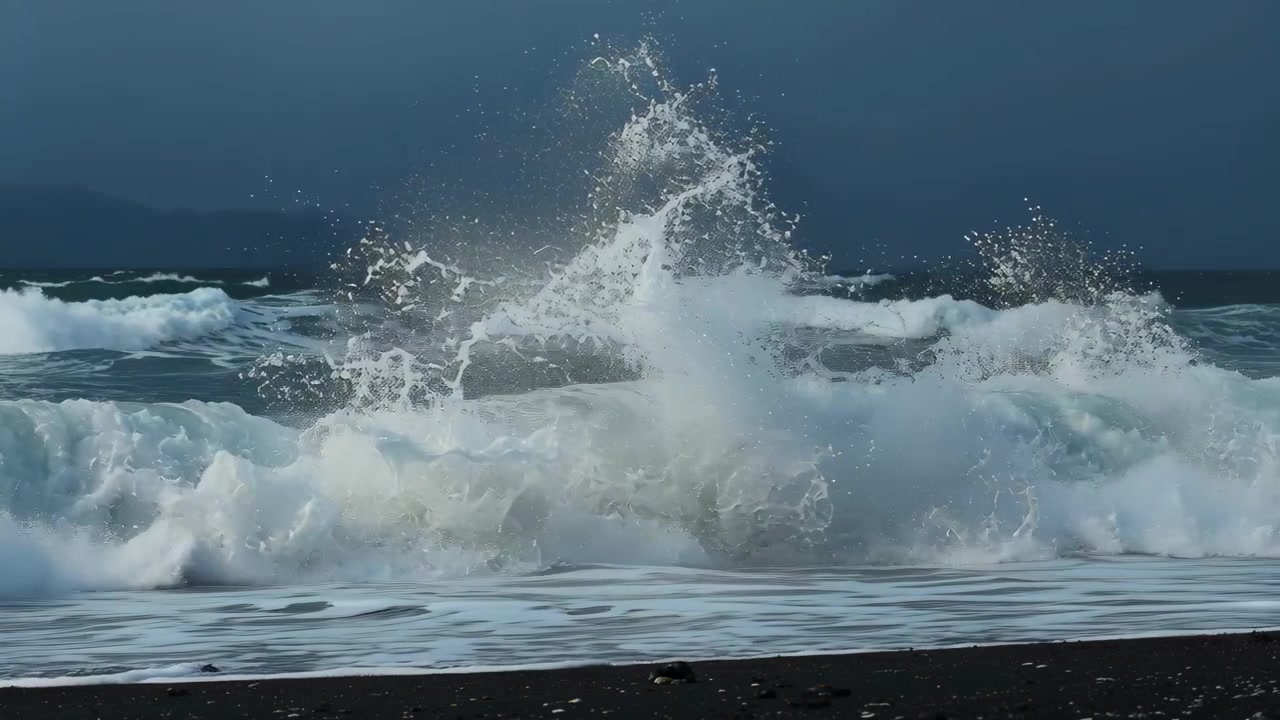 Incoming swell arriving, breaking waves erupting into white spray and pushing foam up dark wet sand