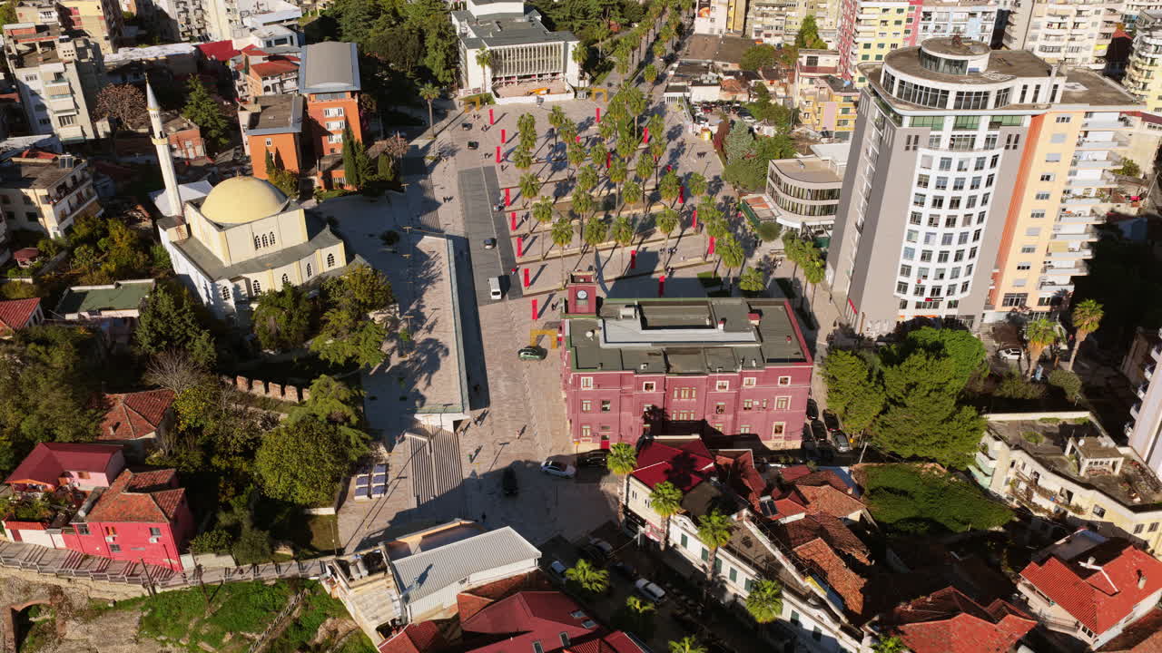 Vista aérea de drone do centro de Durrës, mostrando a Mesquita Islam Iliaz de cúpula amarela, a Praça Liria com fileiras de palmeiras, edifícios residenciais e comerciais ao redor