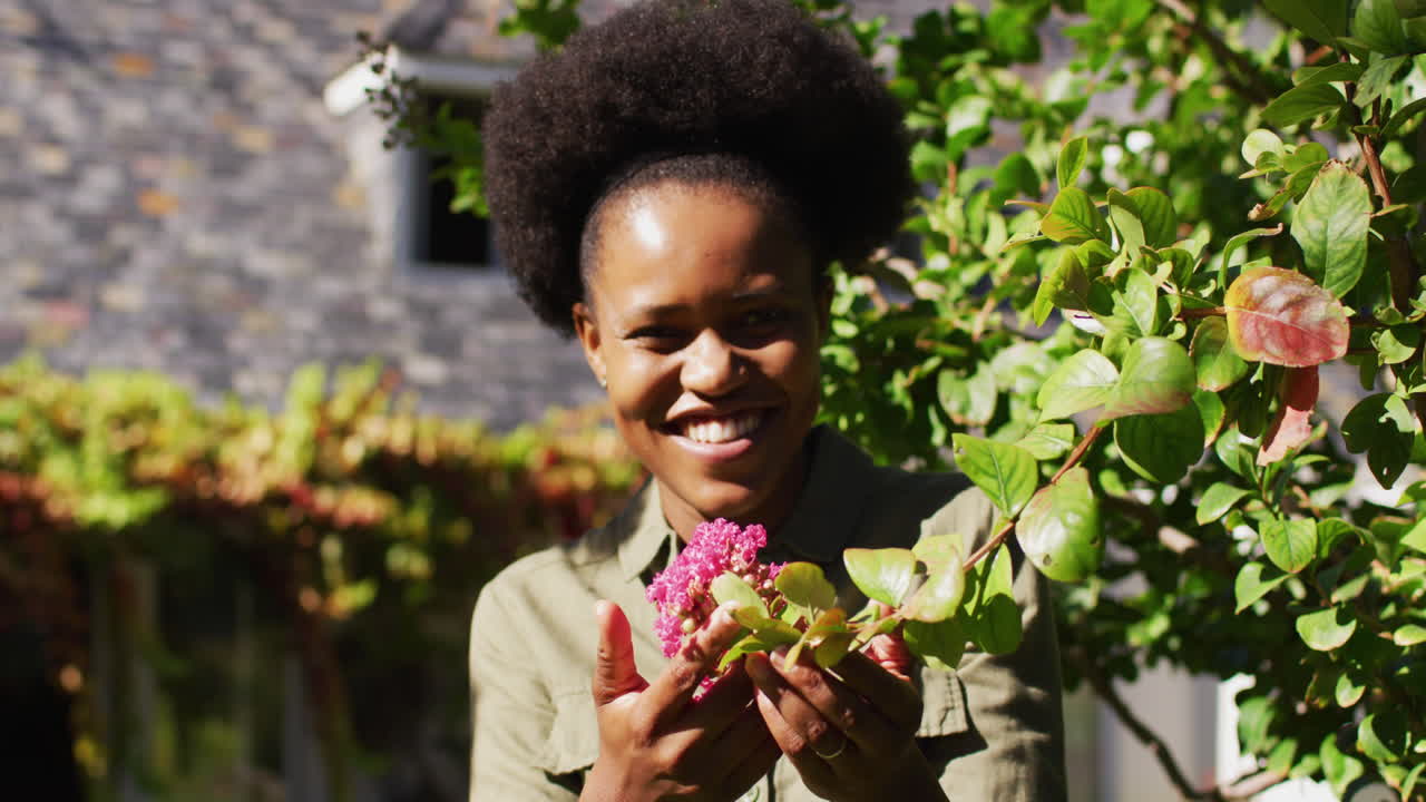 retrato de una mujer afroamericana sonriente de pie en un jardín soleado sosteniendo una planta