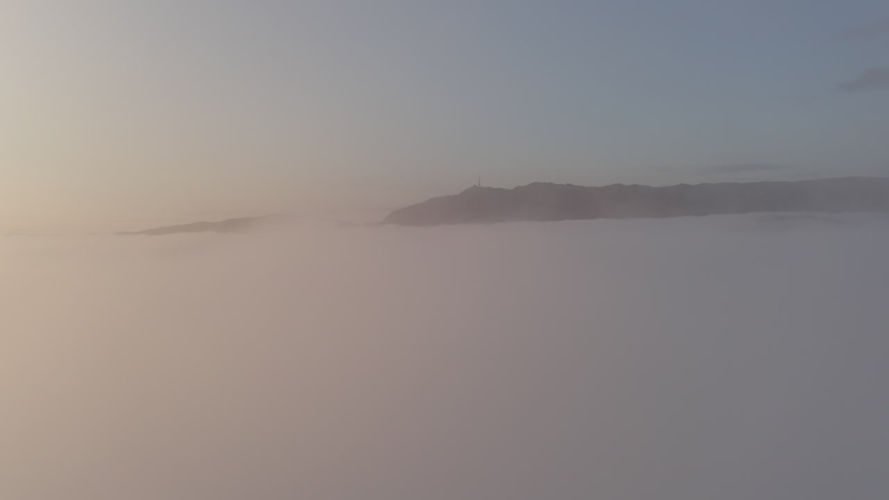 Aerial shot just above a thick layer of fog, showing the mountains peaking up through the clouds.