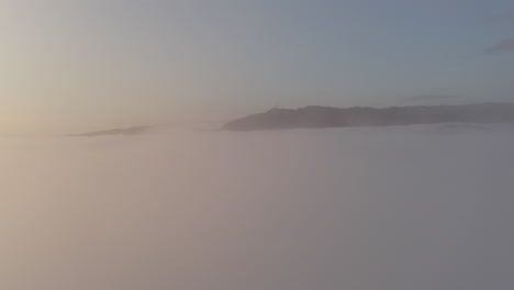 aerial shot just above a thick layer of fog, showing the mountains peaking up through the clouds.