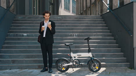 businessman with folding e-bike drinking coffee and using phone