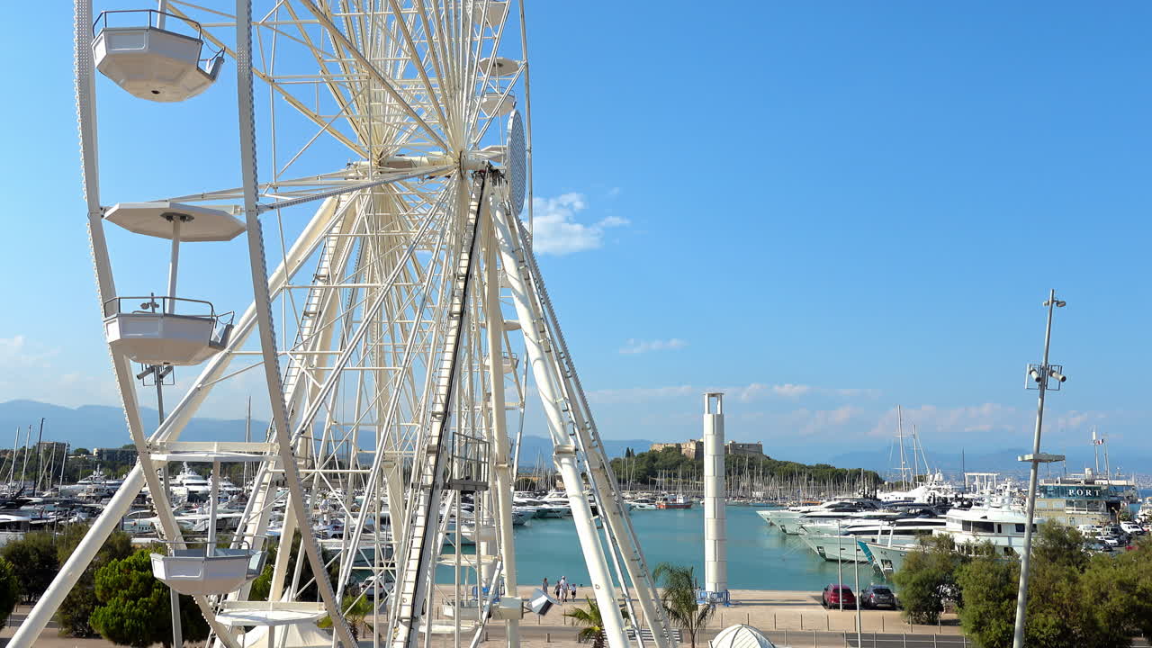 View of white ferris wheel rotating with the sky on the background in Antibes, France
