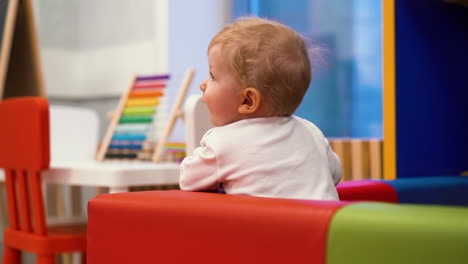 cute little kid leans on soft edge of comfortable playpen