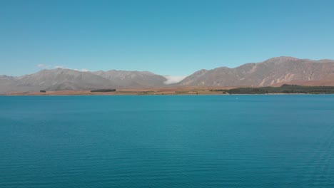 Aerial-shot-of-Lake-Tekapo,-New-Zealand-and-its-Beautiful-Turquoise-Blue-Water-wiht-mountains-in-background