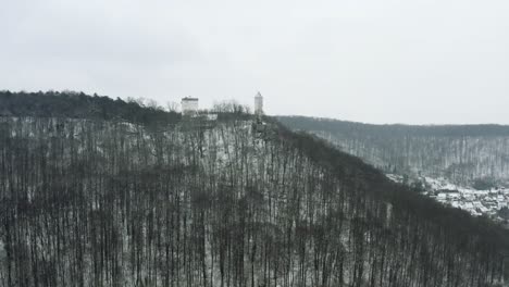 Drone-Aerial-of-the-fairy-tale-castle-Plesse-in-winter-with-a-huge-amount-of-snow-on-a-beautiful-mountain-near-Bovenden,-Germany,-Europe