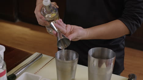 cocktail bartender measuring out alcohol for a mixed drink before pouring it into shaker glass