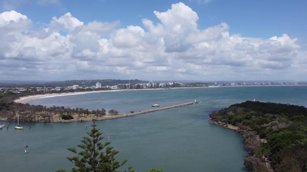 Drone ascending over a bay to reveal an Australian beach town and a nice curved sandy beach in the background