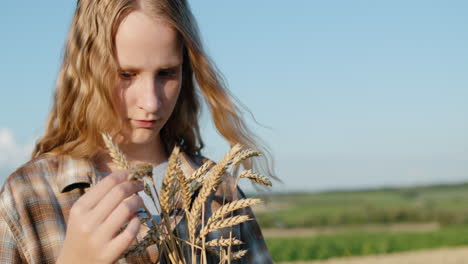 portrait of a teenage girl with spikelets of wheat in her hand. stands against the backdrop of picturesque countryside and wheat fields