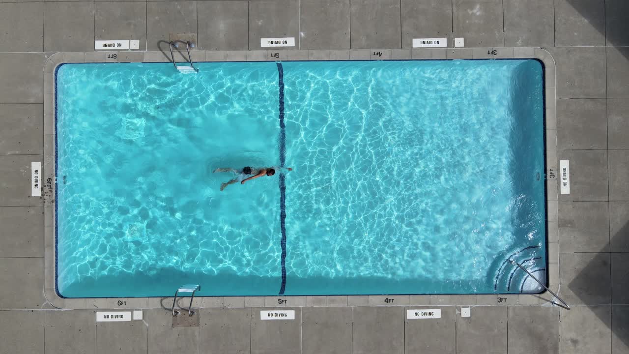 Ovenfra-billede af en mand, der svømmer fra den ene side af en nedgravet pool i baghaven til den anden og tilbage