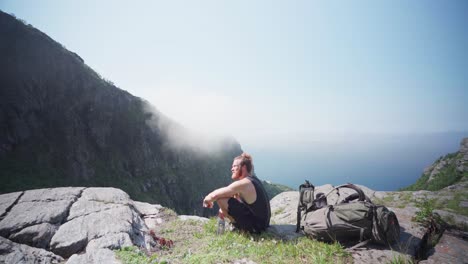 man hiker sits bending his knees on a cliff ledge at mount donnamannen, nordland, norway