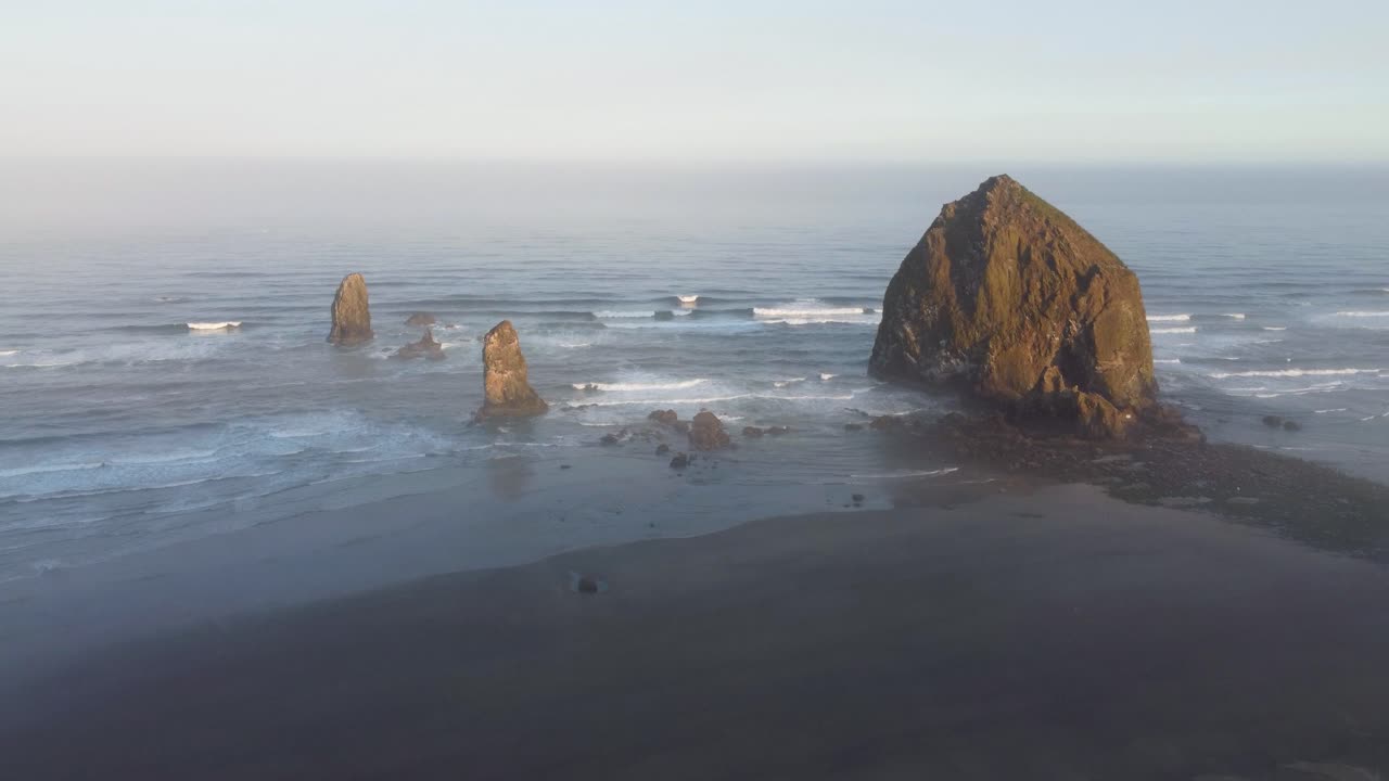 Belo nascer do sol na Costa do Oregon - Rocha Haystack coberta de musgo e água azul cristalina batendo contra a costa do Oceano Pacífico, aves marinhas voando acima. Imagens aéreas de drone 4K 30fps com movimento de aproximação.