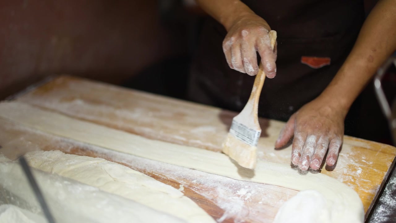 Un venditore di street food spennella farina su lunghe strisce di impasto su un tavolo di legno