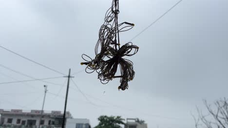 A-close-static-shot-of-water-dripping-from-a-hanging-tangled-string-light-on-a-rainy-day-with-electricity-poles-and-buildings-in-the-background