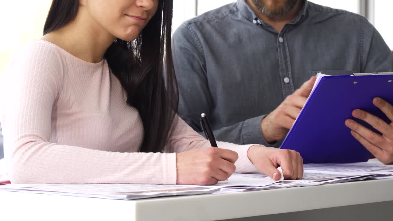 fotografía recortada de una mujer firmando papeles con el vendedor en el salón de automóviles