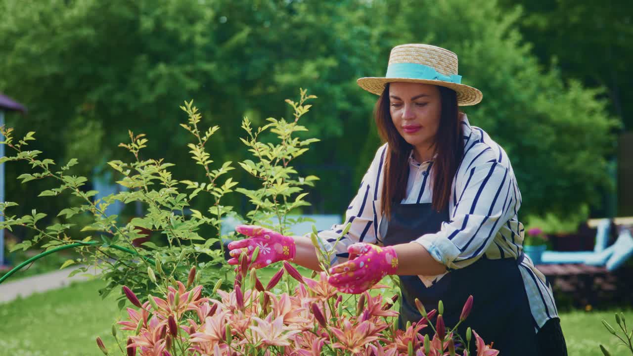 Woman in straw hat tending to vibrant flowers in a sunny garden with lush greenery surrounding