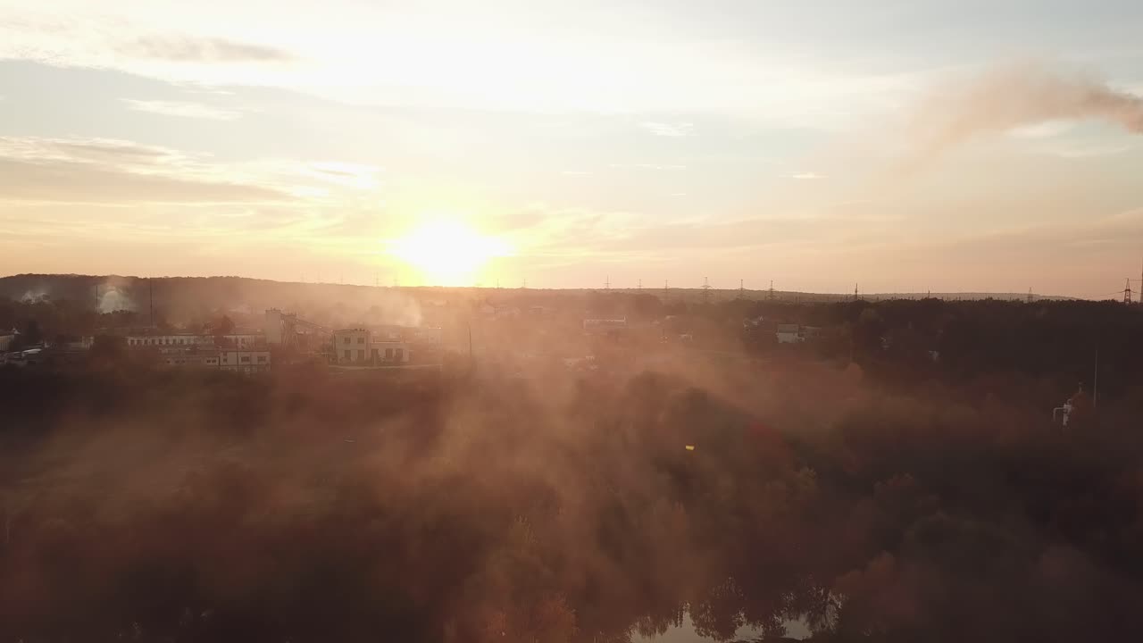 smoke from the fire are soaring over the river and evening city on the background of sunset in the summer. Aerial view