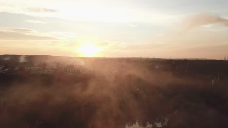 smoke from the fire are soaring over the river and evening city on the background of sunset in the summer. aerial view
