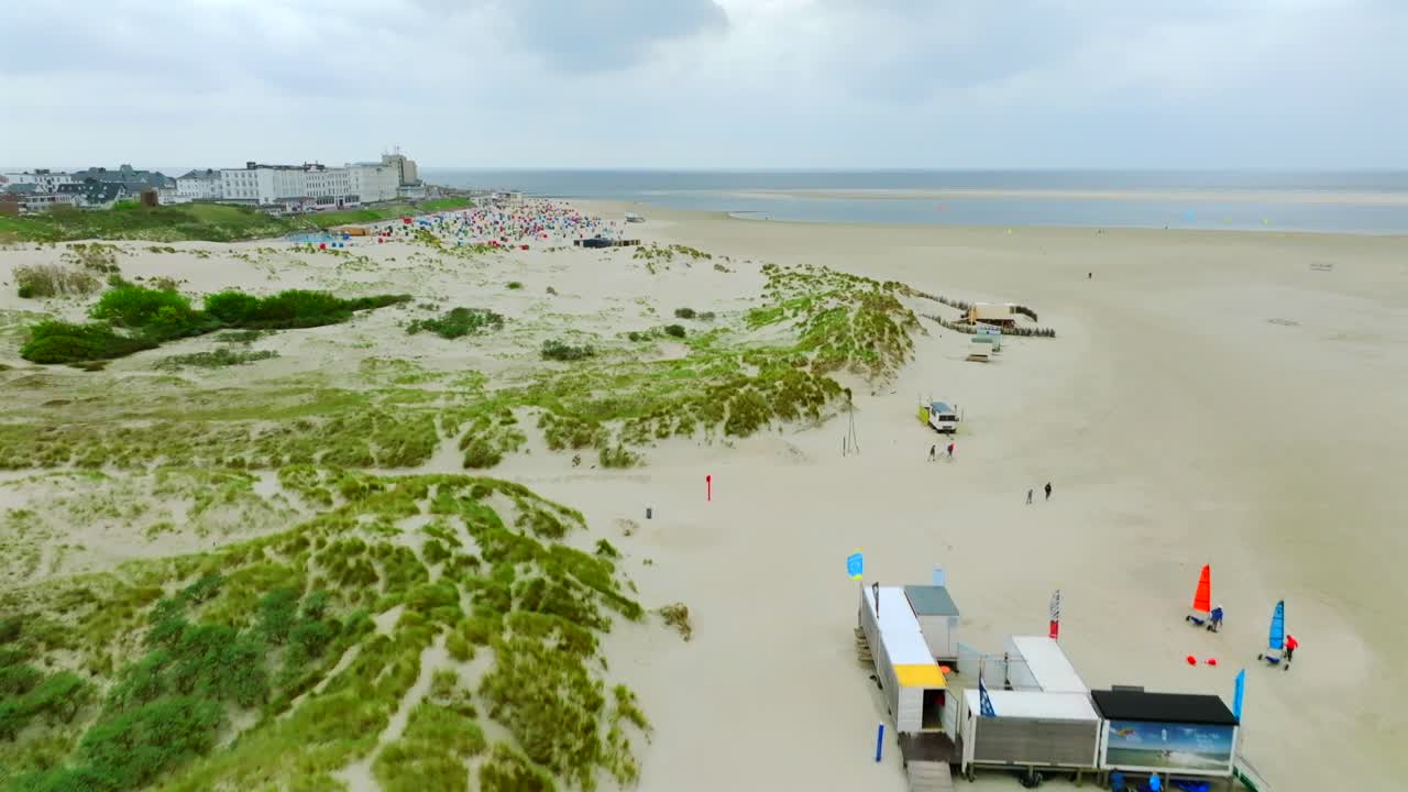 Flyover colorful sand yachts at Borkum island beach. Ascending aerial reveal Borkum town and Wadden sea panorama