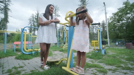 a pregnant mother and her young daughter enjoy playful time together at a playground in the park, surrounded by trees and greenery