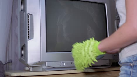 female hand wipes screen of old tv with green microfiber rag and cloth from dust