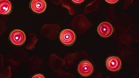 overhead shot of romantic lit red candles revolving on background covered in rose petals 2