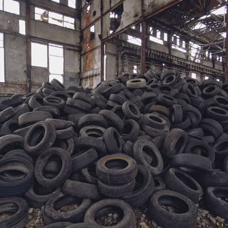 pile of used tires of car are on the ground inside an abandoned factory on the background of the old gray walls. camera motion from down to up.