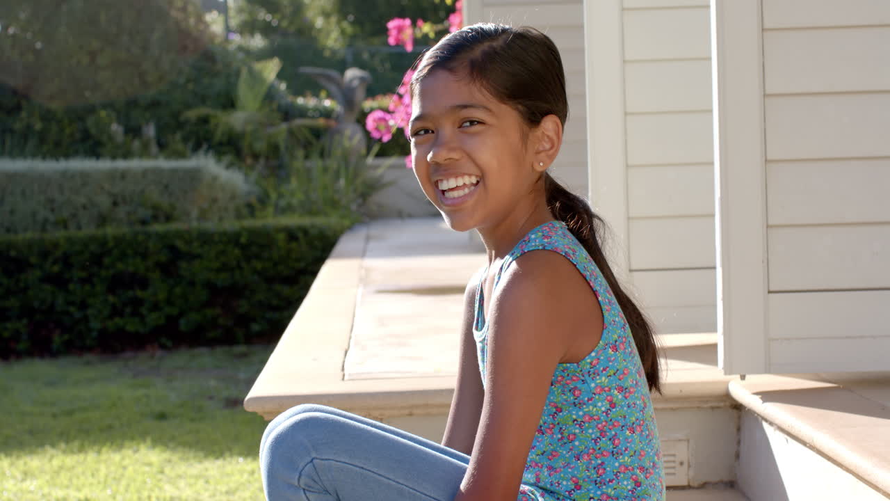 Smiling girl sitting on porch enjoying sunny day at home