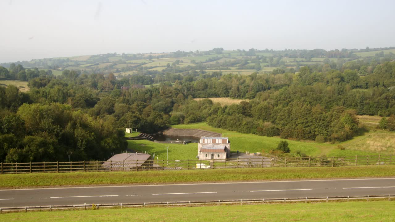 Wide shot of Carsington Water treatment works with the dam road foreground with cars passing through frame
