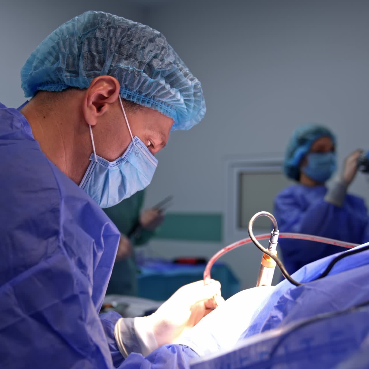 Chirurgo uomo all'opera che utilizza un dispositivo elettrico. Un medico copre il microscopio con della plastica sullo sfondo in modalità sfocata.