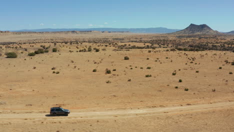 aerial of car driving down dirt road with vast desert landscape in background