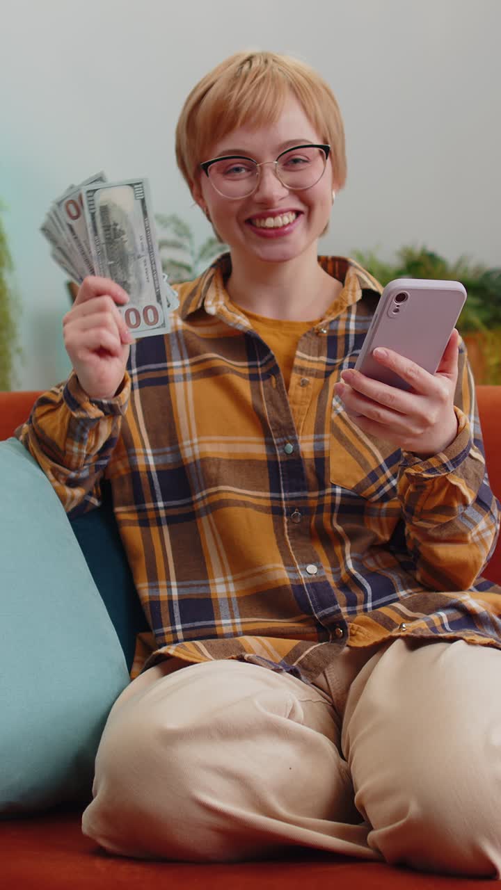Smiling happy young woman counting money cash use smartphone income salary earnings lottery win