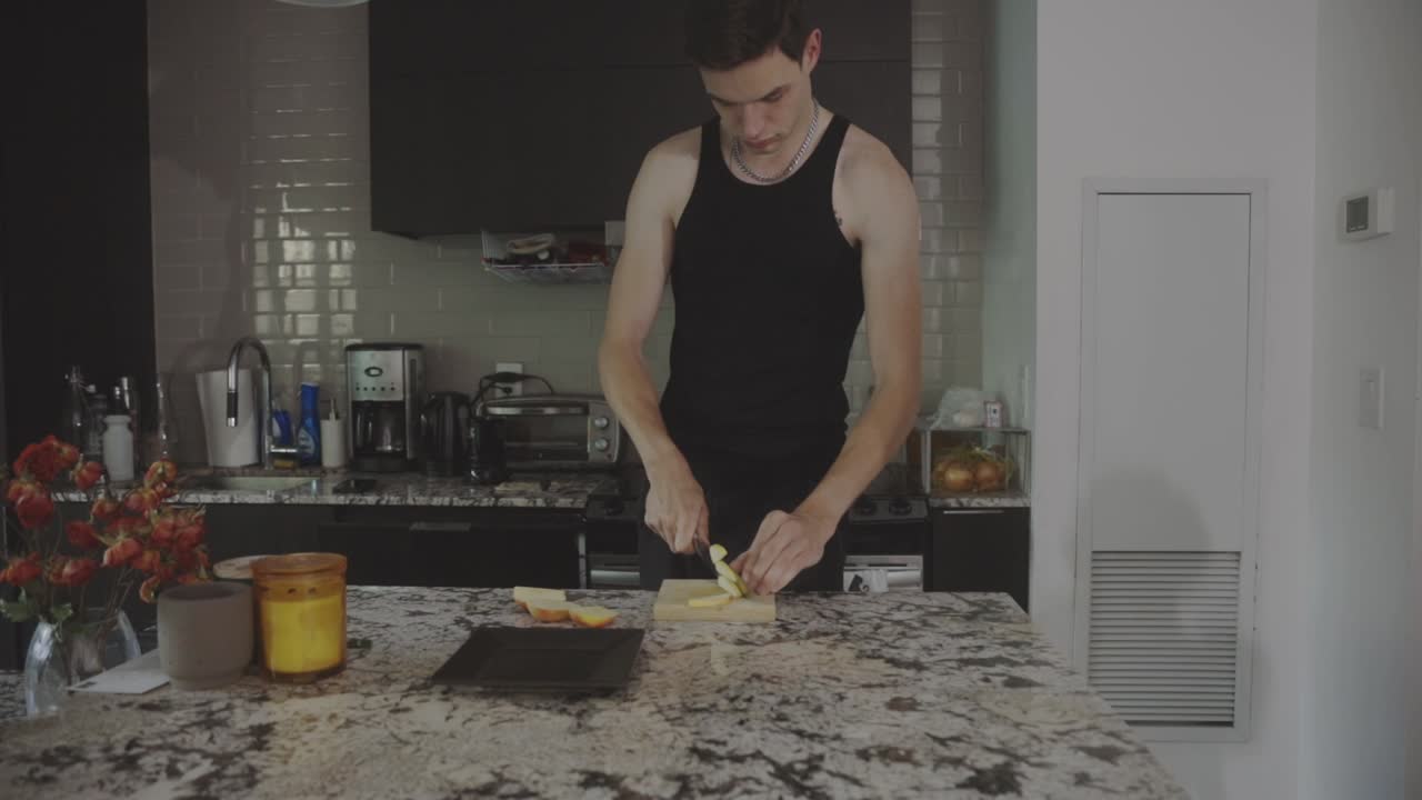 joven hombre caucásico cortando y comiendo fruta de manzana fresca en el mostrador de la cocina