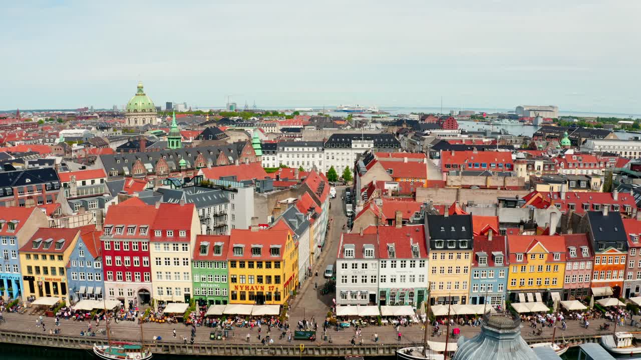Et droneperspektiv af Nyhavns kanal, med farverige byhuse og fodgængere, der går langs vandet