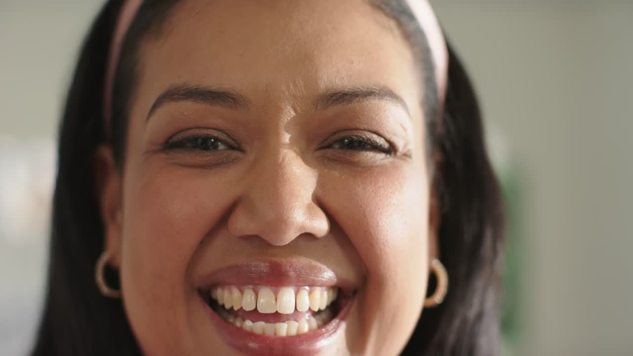 African American woman smiling then laughing after offscreen joke at home, pink headband gold hoops