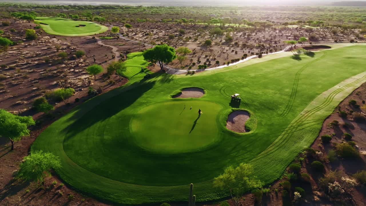 Aerial shot of a greenskeeper putting the flagstick in on a desert green surrounded by bunkers and dramatic early morning shadows