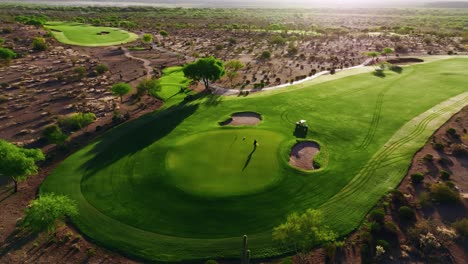 aerial shot of a greenskeeper putting the flagstick in on a desert green surrounded by bunkers and dramatic early morning shadows