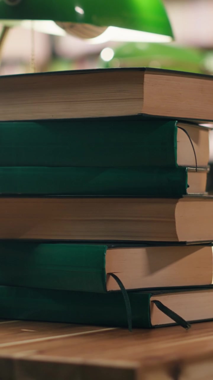 Vertical Video Close up green books in piles placed on table desk in library under green lamps