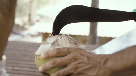 A-man-is-opening-a-coconut-with-a-machete-in-a-Goa-neighborhood,-India