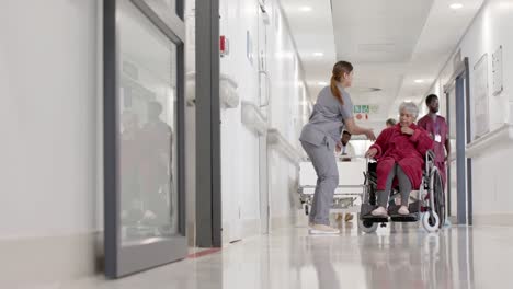 serious diverse female nurse walking with senior patient in wheelchair in slow motion, unaltered