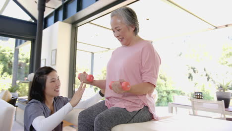 assisting senior asian woman with dumbbells, physiotherapist encouraging during home workout