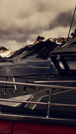 dark-colored boat in front of snowy mountains