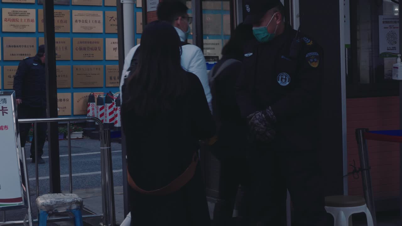 A masked security guard in front of a Chinese hospital stops people to check their digital health codes upon entering. COVID-19 pandemic safety measures in China.
