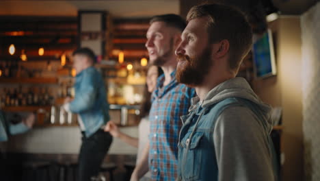 a group of men and women in a pub cheering for their national team at the world cup. enjoys scoring a goal while sitting at the table with a beer. fans celebrate a goal by watching tv in a bar