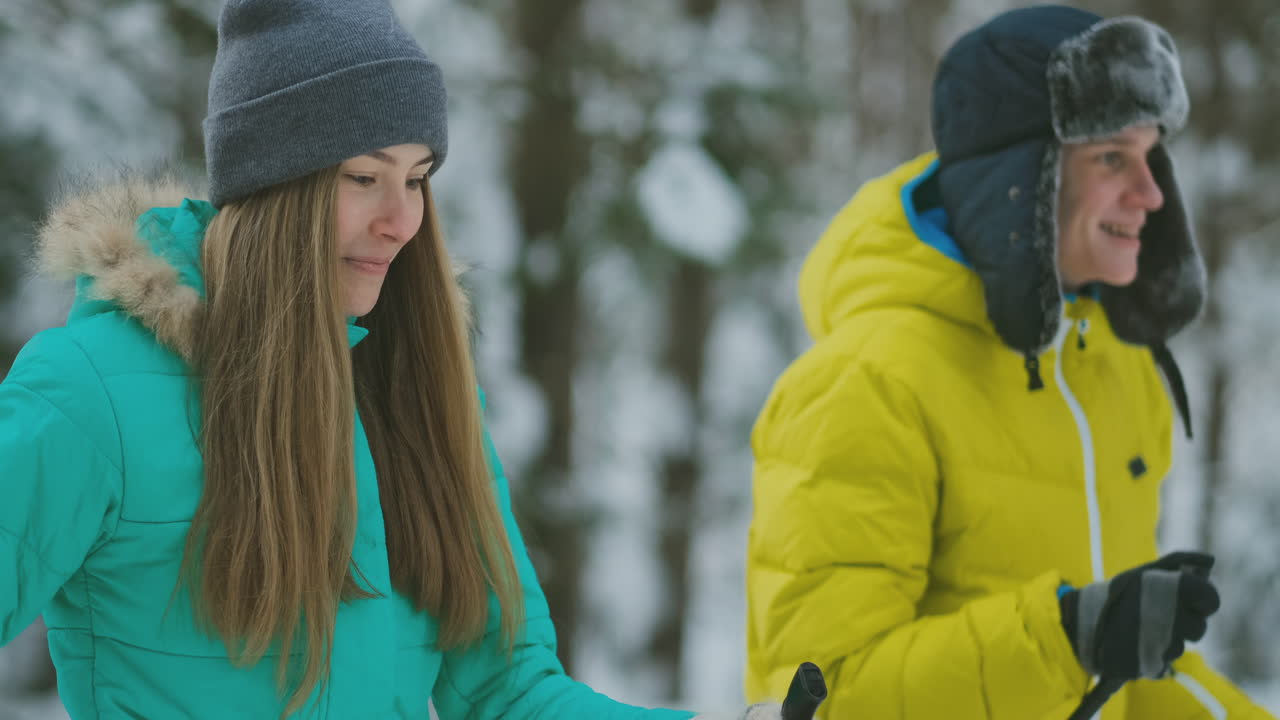 Ritratto di una coppia sposata. Un uomo con una giacca gialla e una donna con una tuta blu in inverno nel bosco, mentre sciano al rallentatore.