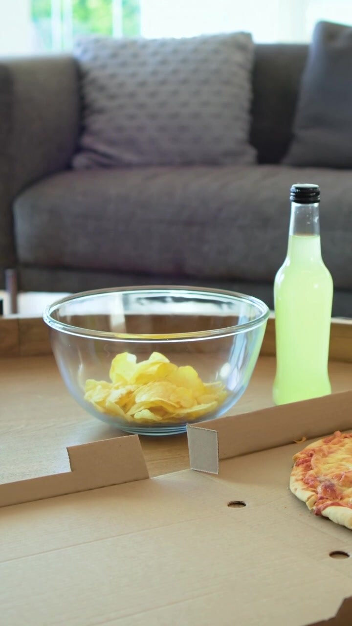 Vertical video: Pulling back camera revealing chips on table at home to show pizza and lime bottles