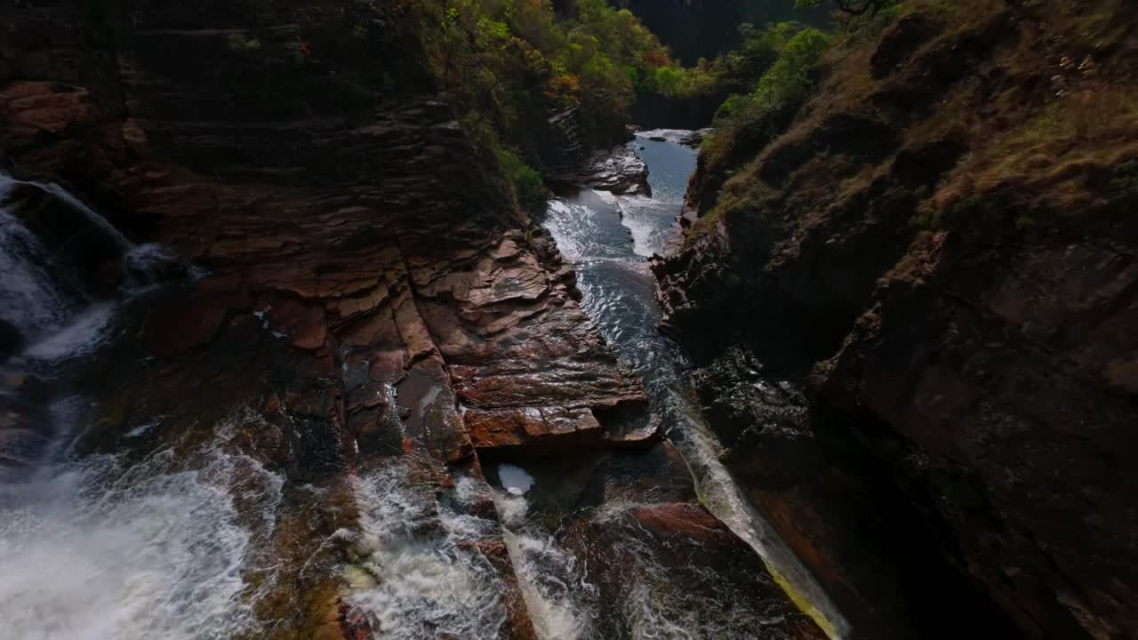 Stunning aerial perspective of cascading waterfalls flowing over rocky terrain in Chapada dos Veadeiros National Park, Goiás, Brazil. Lush greenery surrounds the vibrant, rushing water