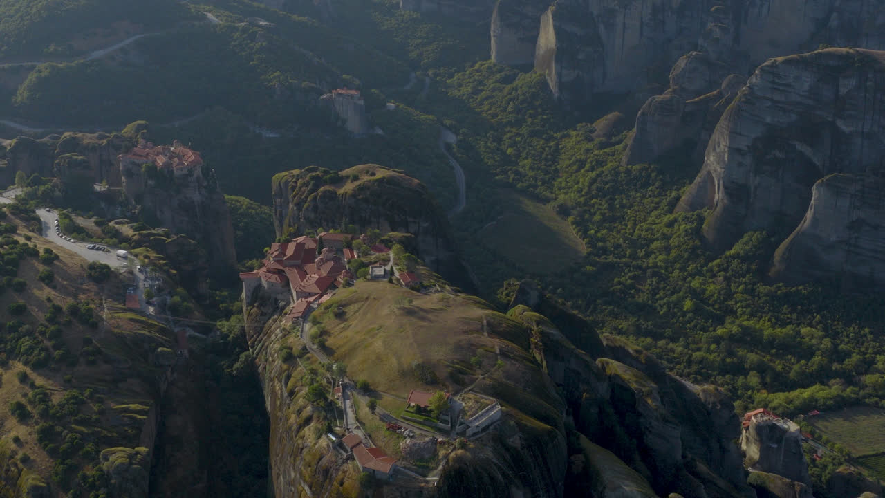 Cinematic aerial view of Meteora monastery in Greece perched on towering cliffs, dramatic rock formations and lush green valley create a breathtaking historic scene