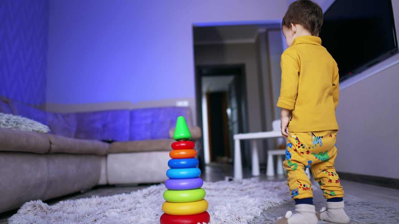 Cute toddler collected the pyramid and stands up walking around it. Baby comes up to the toy and turns it upside down.