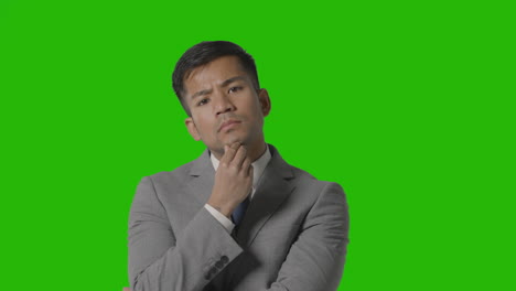 portrait of serious businessman in suit thinking against green screen looking at camera